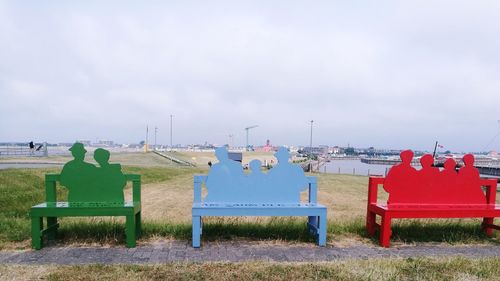 Rear view of people sitting on bench on field against sky