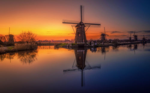 Traditional windmill by lake against sky during sunset