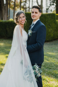 Portrait of bride and groom standing on grass in park
