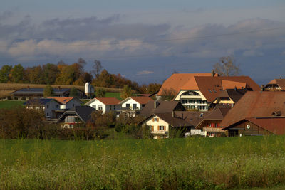 Houses on field by buildings against sky