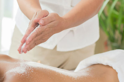 Midsection of therapist pouring talcum powder on woman back at health spa