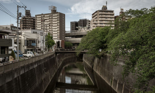 Bridge over river amidst buildings in city against sky