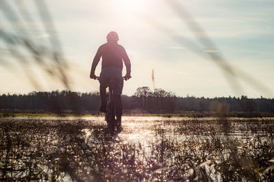 Rear view of man riding bicycle on grass against sky