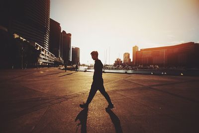 Side view of man walking on street in city against sky during sunset