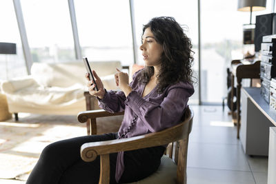 Businesswoman using smart phone sitting on chair in office