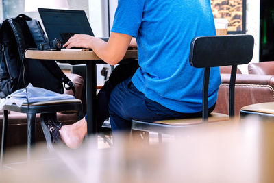 Low section of man working on laptop at table in cafe