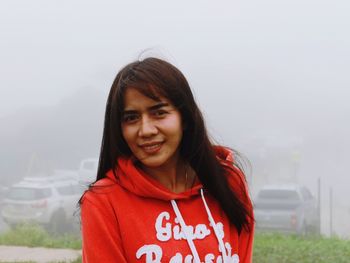 Portrait of woman smiling while standing against city during foggy weather