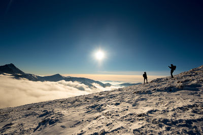 People on snowcapped mountain against sky during winter