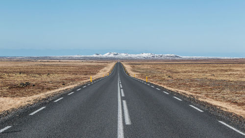 Empty road passing through landscape against clear sky