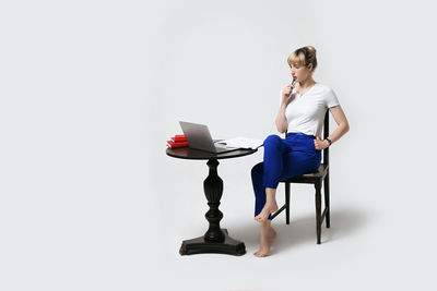 Young woman using laptop while sitting against white background