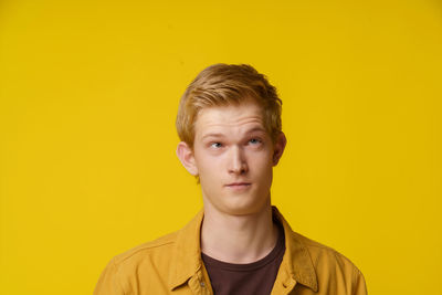 Portrait of young woman standing against yellow background