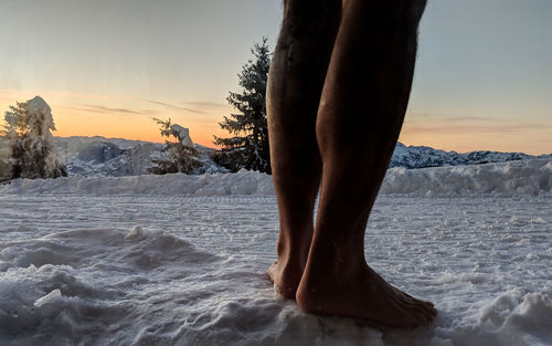 Low section of person standing on snow covered land during sunset