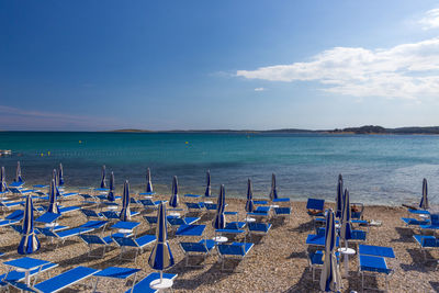 Deck chairs on beach against sky