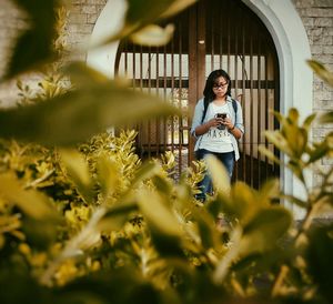 Young woman using smart phone standing against gate