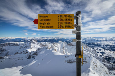 Road sign on snow covered landscape against sky
