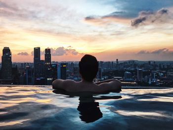 Rear view of man in infinity pool against cityscape