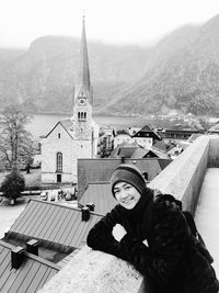 Portrait of young woman on terrace against church amidst houses at hallstatt
