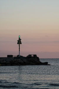 Lighthouse by sea against sky during sunset