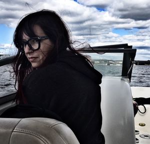 Portrait of young woman sitting in boat against cloudy sky