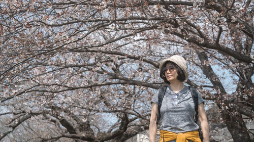 Portrait of young woman standing against bare tree