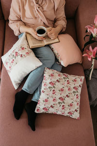 High angle view of woman reading book sitting on sofa at home