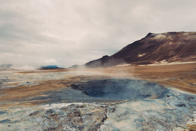 Steam emitting from volcanic landscape against cloudy sky