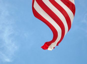 Low angle view of striped american flag waving against blue sky