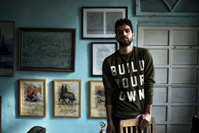 Portrait of young man standing against picture frames at home