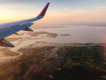 Airplane flying over sea against sky during sunset