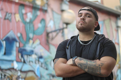 Portrait of young man with arms crossed standing against building