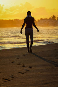 Rear view of man standing on beach during sunset