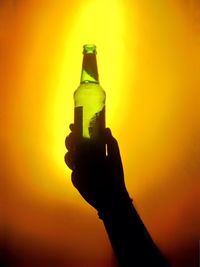 Close-up of hand holding bottle against orange sunset