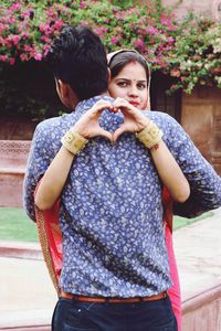 Portrait of woman making heart shape while embracing with man outdoors