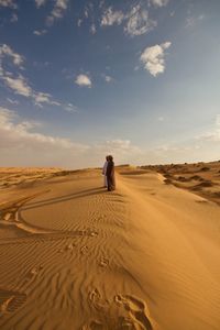 Men standing in arid landscape against sky on sunny day