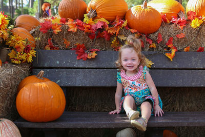 Portrait of girl smiling on bench by pumpkins at park during autumn