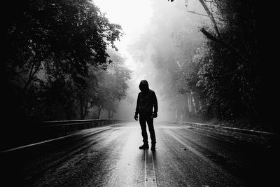 Black and white image a man standing on empty road during foggy weather