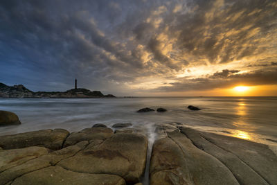 Scenic view of beach against cloudy sky during sunset