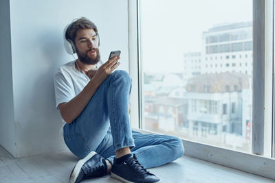 Young man using mobile phone while sitting on window