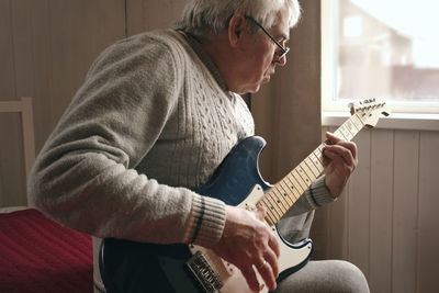 Senior man is playing guitar. elderly man sitting on the sofa and playing guitar. portrait of a gray