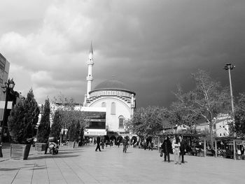 People walking in city against cloudy sky