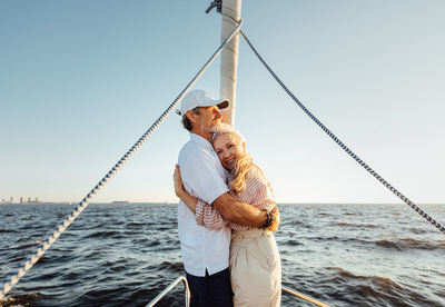 Senior couple embracing while standing on boat against sea