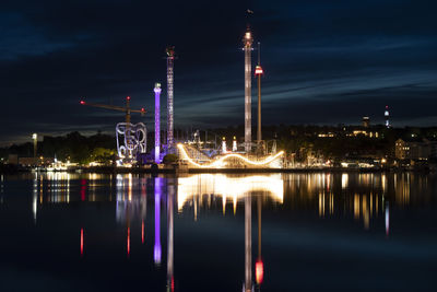 Illuminated city by river against sky at night