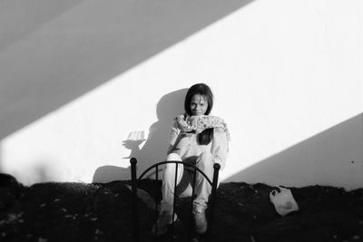 Full length portrait of young woman sitting with wine by wall