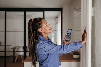 Smiling woman touching radiator standing with smart phone at home