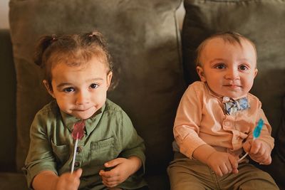 Cute siblings eating candy while sitting on sofa at home