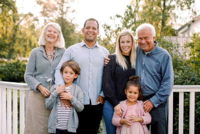 Portrait of smiling multi-generation family standing against railing in backyard