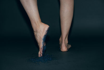 Low section of woman walking on glitter over gray background