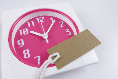 Close-up of blank label on pink clock over white background