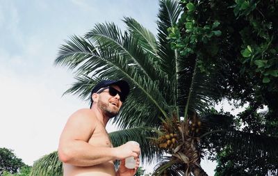 Portrait of shirtless man with palm tree against sky