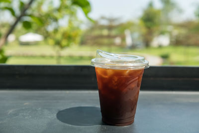 Ice americano black coffee on table with spring garden view of outdoor cafe and restaurant.